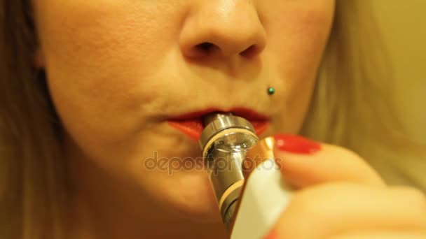 La chica fuma un vaporizador electrónico de cigarrillos y libera vapor de humo de su boca
. - Metraje, vídeo