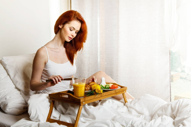 Young woman eats breakfast in bed in the morning - Фото, изображение
