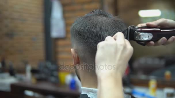 The hands of young barber making haircut to attractive man in barbershop - Imágenes, Vídeo