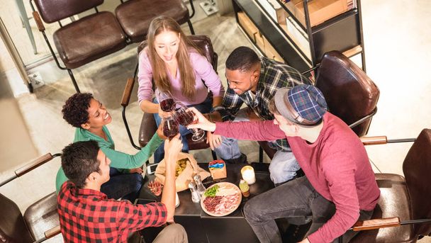 Top side view of multi racial friends tasting red wine and having fun at cool fashion bar winery location - Multicultural trendy friendship concept with people enjoying time out drinking together - Фото, зображення