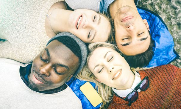 Top view of multiracial best friends having fun resting together outdoors on sunny day - Happy friendship and peace concept with young multicultural people on relax mood - Bright vintage filtered look - Photo, Image