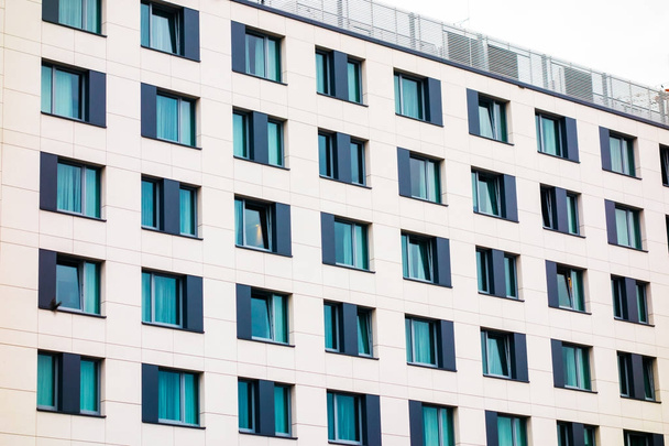 Современный коммерческий фасад здания с рядами повторяющихся квадратных окон с голубыми тонированными шторами в белой стене просматривается под низким углом
 - Фото, изображение