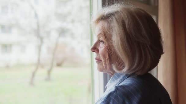 ηλικιωμένη γυναίκα κοιτάζει έξω από το παράθυρο - Πλάνα, βίντεο
