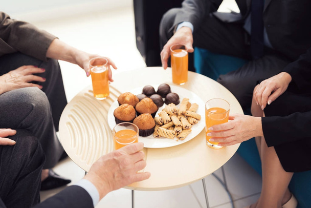 Plate of cookies and four glasses of orange juice on a round table. Four hands reach for the glasses. - Fotó, kép