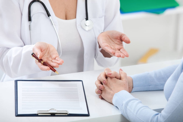 Лікар і пацієнт щось обговорюють, тільки руки за столом крупним планом
 - Фото, зображення
