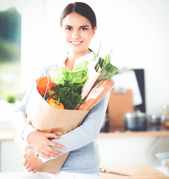 Young woman holding grocery shopping bag with vegetables . Standing in the kitchen - Foto, Imagem