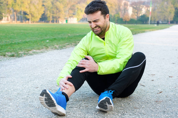 Atleta masculino que sufre de dolor en la pierna mientras hace ejercicio al aire libre
 - Foto, imagen