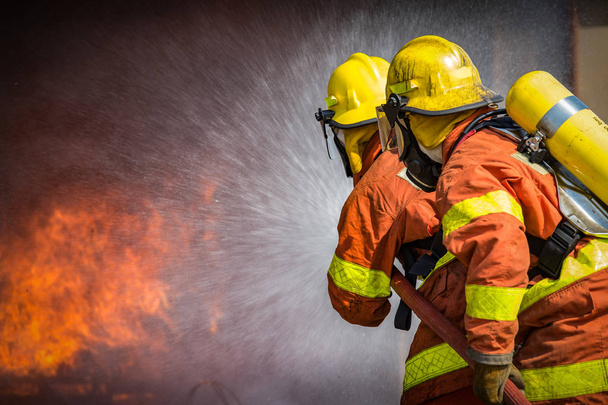 2 Feuerwehrleute versprühen Hochdruckwasser, um Feuer mit Kopierraum zu löschen - Foto, Bild