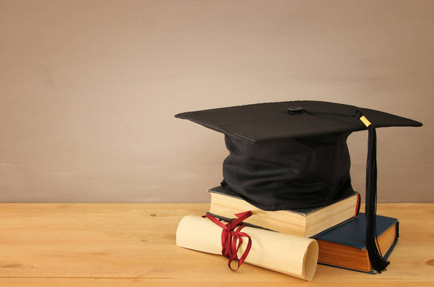 Image of graduation black hat over old books next to graduation on wooden desk. Education and back to school concept - Foto, Imagen