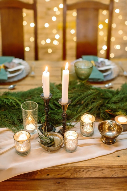 tableware, eco style, feast concept. table served for celebrating christmas and decorated with numerous of candles with warm fires and fresh conifers brunches placed in the center of it - Valokuva, kuva