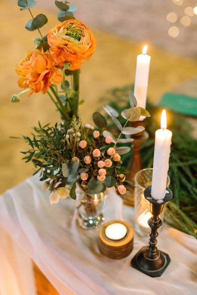 feast, present, floral design concept. on thick drapping two small extremely beautiful posies with bright orange roses, lots of various leaves and small light pink berries, they are placed by candles - Valokuva, kuva