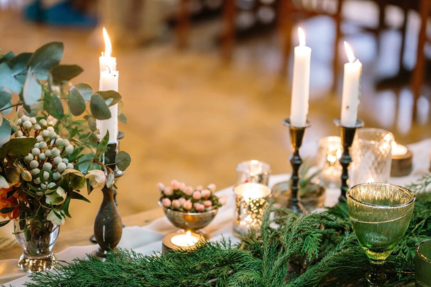 christmas, presents, celebration concept. bright fires of feast candles that decorat the table, they are lightening posies of various leaves and bright conifer branches in fresh green colour - Photo, image