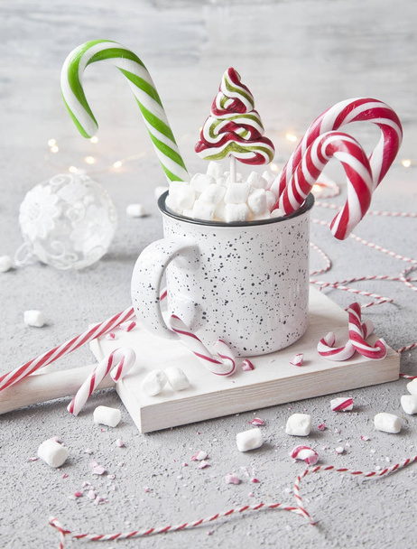 close-up of white hot drink in mug with marshmallow and candy canes, Christmas decor on grey background. Christmas concept. - Photo, image