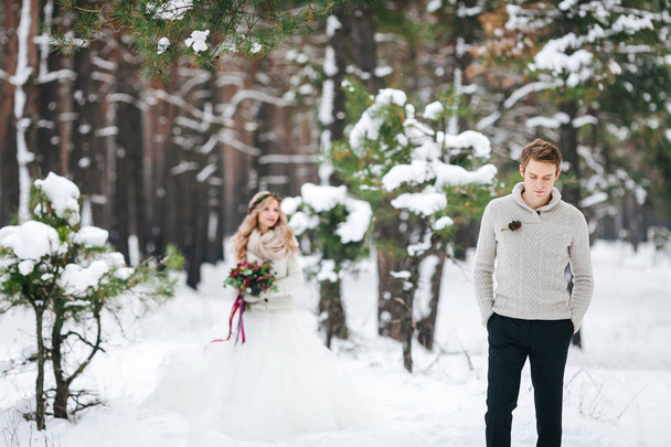 Handsome groom in beige pullover on background of blurred bride in snowy forest. Winter wedding. Artwork. - 写真・画像