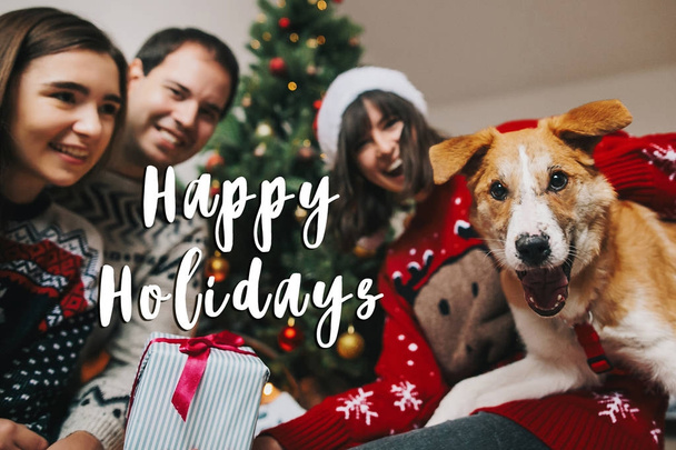 gelukkige familie vieren van Kerstmis met grappige hond in ingerichte kamer en Happy Holidays tekst - Foto, afbeelding