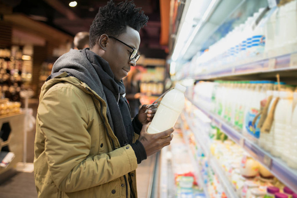 African man holding and choice milk or yogurt bottle in supermarket showcase, healthy food concept - Zdjęcie, obraz