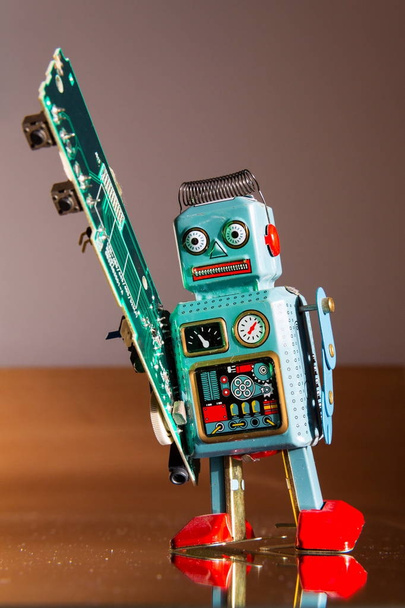 Kızgın vintage teneke oyuncak robot yeşil bilgisayar devre kartı, yapay zeka kavramı taşır - Fotoğraf, Görsel