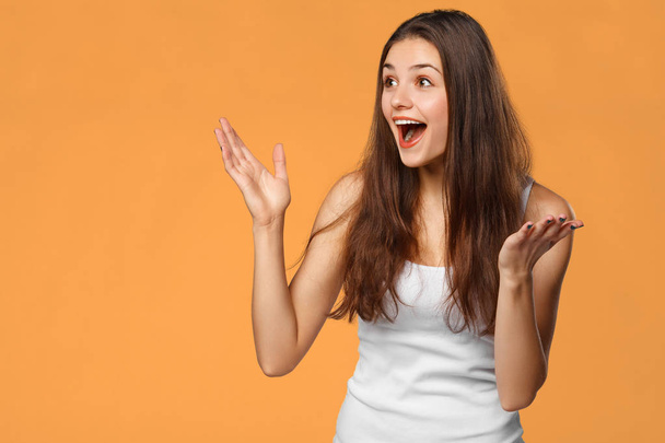 Surprised happy beautiful woman looking sideways in excitement, isolated on orange background - Photo, Image