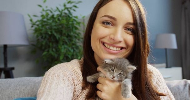 Portrait of a pretty young woman hugging a cute kitty and posing funny to the camera in the cozy room at home. Indoor - Photo, Image