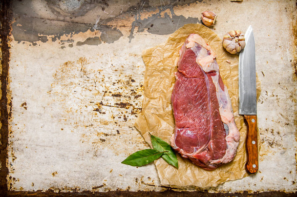 Fresh raw meat with a large knife and a Bay leaf. - Zdjęcie, obraz