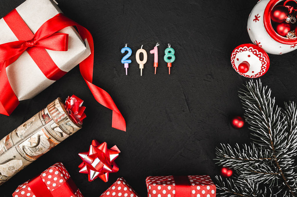Vista dall'alto superiore di un nastro rosso, presente, giocattolo Babbo Natale fatto a mano e ramo sempreverde su uno sfondo nero pietra, con candele numero 2018
 - Foto, immagini