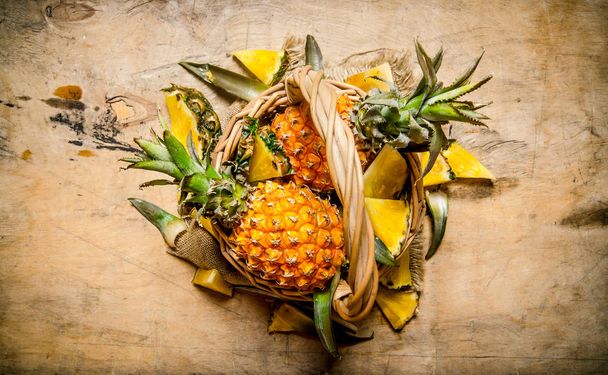 Fresh pineapples in the basket. On wooden table. - Φωτογραφία, εικόνα