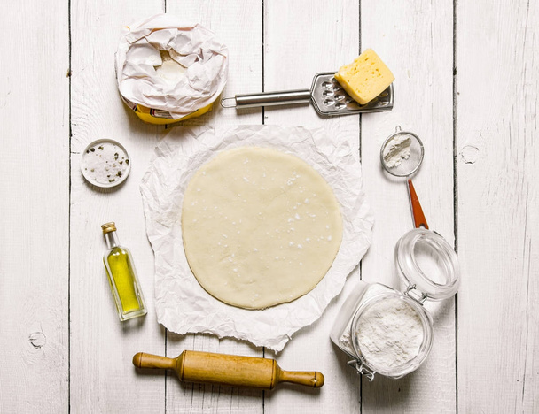 Roll-out de pizza deeg en ingrediënten - bloem, kaas, olivkovoe olie.  - Foto, afbeelding
