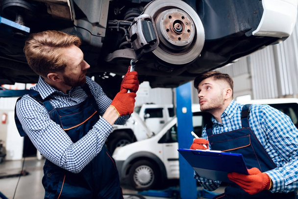 Father and son work at the auto service. Two mechanics work with the details of the car. - Foto, Bild