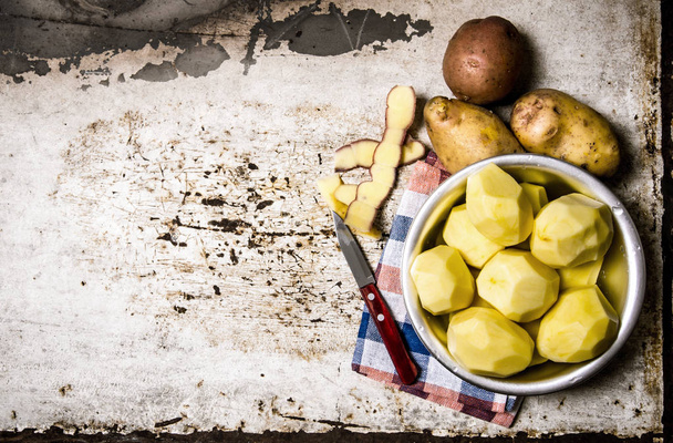 The peeled potatoes in a metal bowl on the rustic background . Free space for text. - Photo, Image