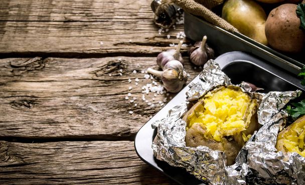 Baked potatoes in foil with salt and garlic on a wooden table . Free space for text. - Valokuva, kuva