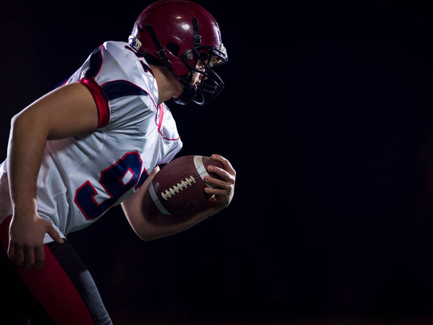 American football player holding ball while running on field - Foto, imagen