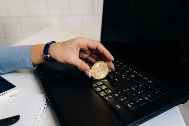 girl financier working on a laptop, holding a gold bitcoin in her hand - Fotoğraf, Görsel