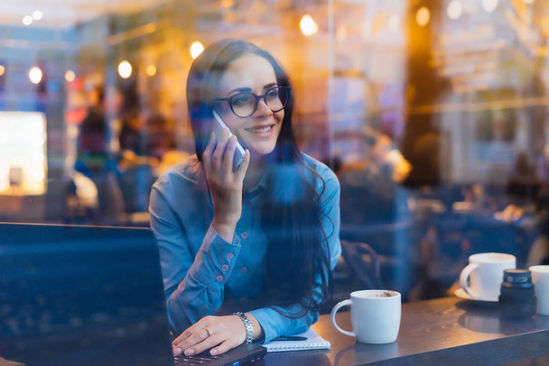 szczęśliwy udany biznes kobietę w okularach siedzi w kawiarni, rozmawiając przez telefon - Zdjęcie, obraz