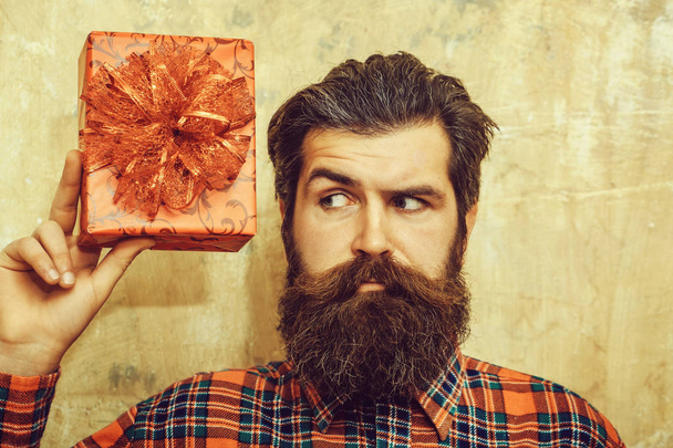 Нахмуренный бородатый мужчина держит красную подарочную коробку с луком
 - Фото, изображение