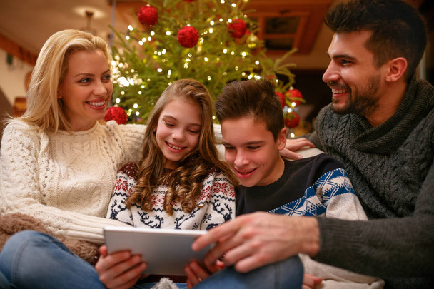 Family having fun while looking Christmas photos together - 写真・画像