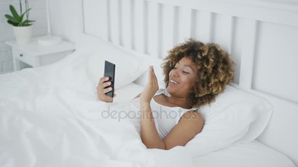 Smiling woman in bed talking online - Video