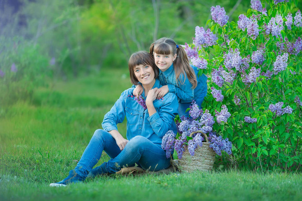 Cute adorable beautifull mother lady mom woman with brunette girl daughter in meadow of lilac purple bush.People in jeans wear. - Foto, Bild