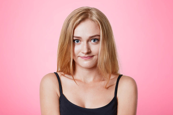 Beautiful young female model with appealing appearance, light straight hair, dressed casually, looks confidently directly into camera, isolated over pink background, spends free time at home - Foto, afbeelding