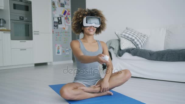 Cheerful sportswoman in VR glasses at home - Filmati, video