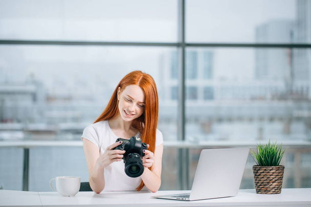 redhead woman looking at camera while working on laptop - Фото, зображення