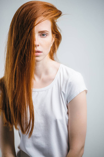 young pretty redhead girl with freckles looking at camera smiling touching hair - Fotó, kép