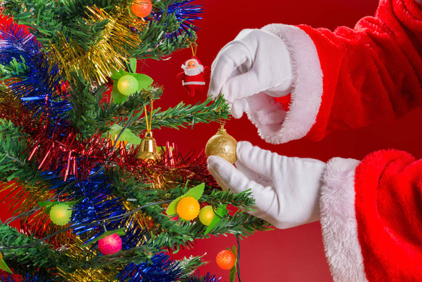 Santa Claus hanging Christmas ball to a fir tree - Foto, imagen