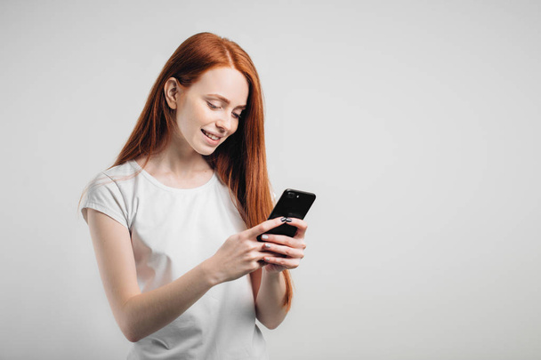 Portrait of a smiling redhead woman holding smartphone and texting - Φωτογραφία, εικόνα