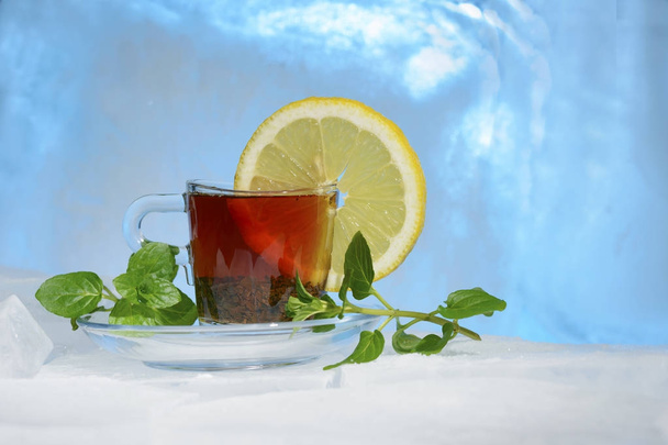 чашка крепкого черного чая на красивом голубом льду с желтым лимоном и зеленой мятой
 - Фото, изображение