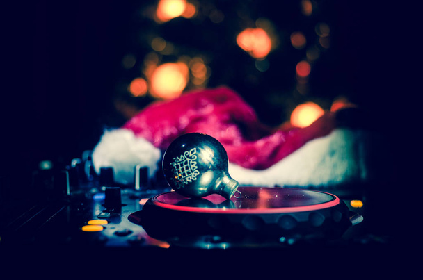Dj mixer con cuffie su sfondo nightclub scuro con albero di Natale Capodanno. Vista da vicino di elementi o simboli di Capodanno (Babbo Natale, Pupazzo di neve, Cane 2018, confezione regalo) su un tavolo Dj. tonica
 - Foto, immagini