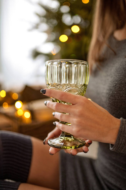 Closeup of glass of wine in hands of young woman on background of celebratory lights. - Foto, afbeelding