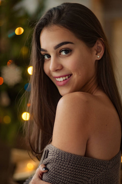 Portrait of beautiful young woman with bare shoulder on background of Christmas lights. Side view. - Photo, Image
