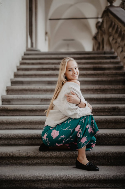 Stylish happy blonde young woman sitting on the stairs. - Zdjęcie, obraz