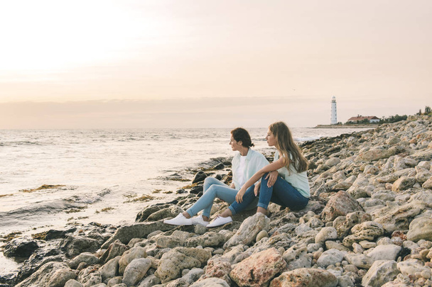 Mom and her teenage daughter relaxing together over sunset sea view - Foto, Imagen