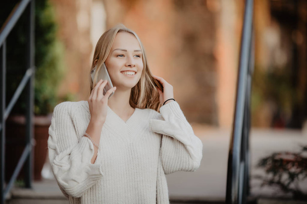 beautiful young blonde woman walking on the street and talking on a cell phone,the girl laughs and smiles. - Photo, image
